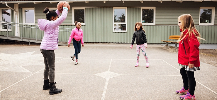 Four children playing basketball in a schoolyard.